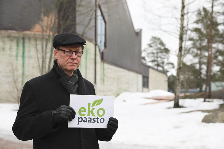 Kari Larjava pitää kädessään Ekopaasto-kylttiä. Taustalla Espoonlahden kirkko.