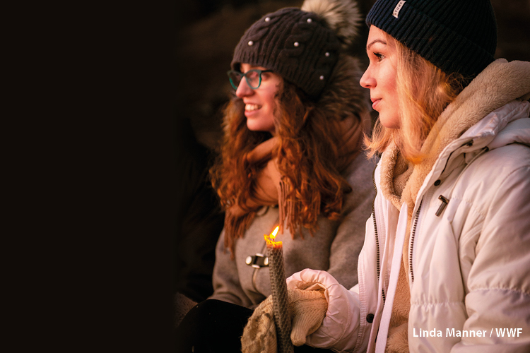 Kuvassa on kaksi nuorta naista talvivaatteissa. Toisella henkilöllä on kädessään palava kynttilä. Kuva: Lin...