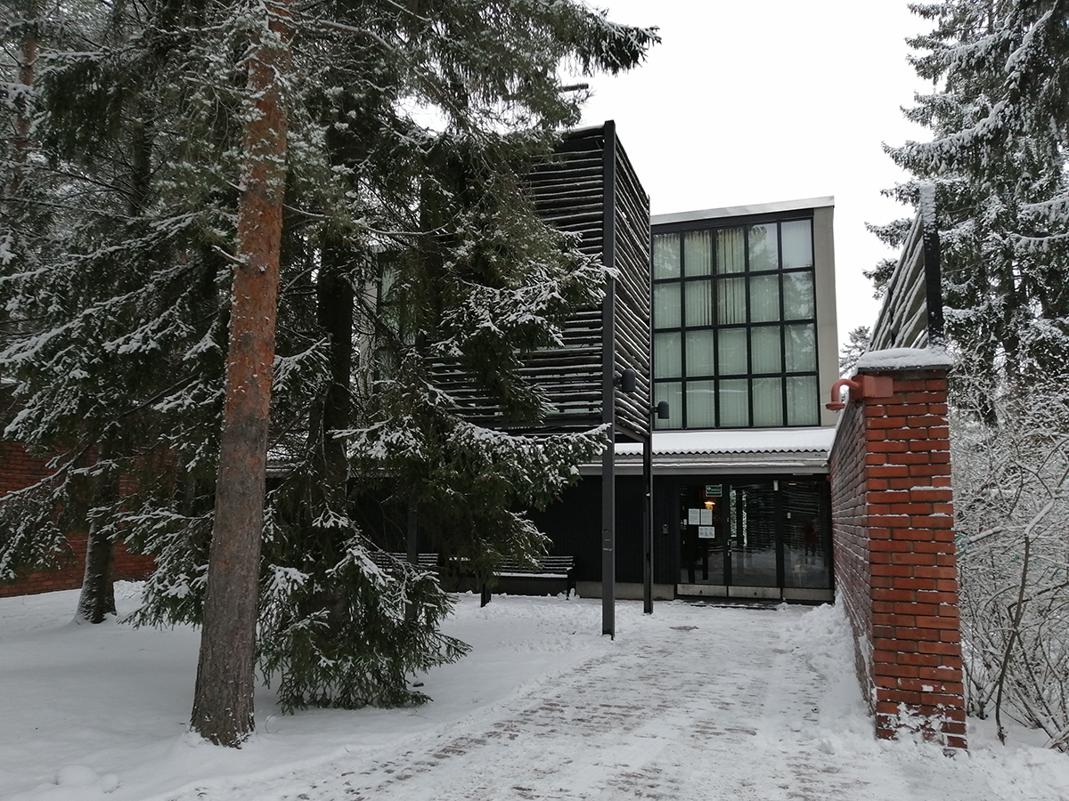 Otaniemen punatiilinen kappeli lumisten puiden keskellä.