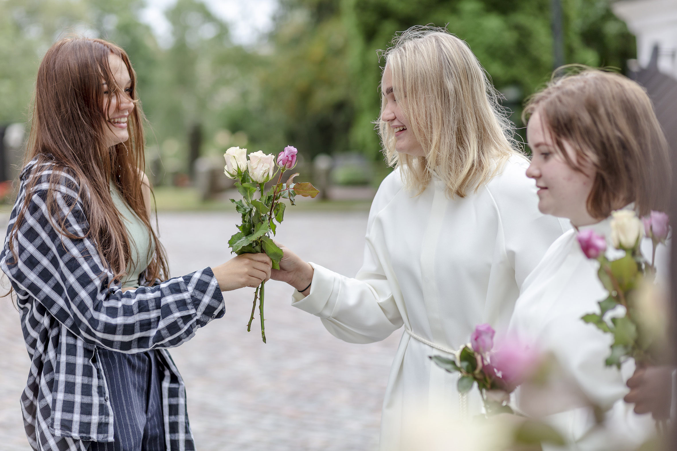 Kuvassa alboihin pukeutuneen nuoret ojentavat ruusuja toisilleen. Rippikoulut pystyttiin pitämään koronapan...