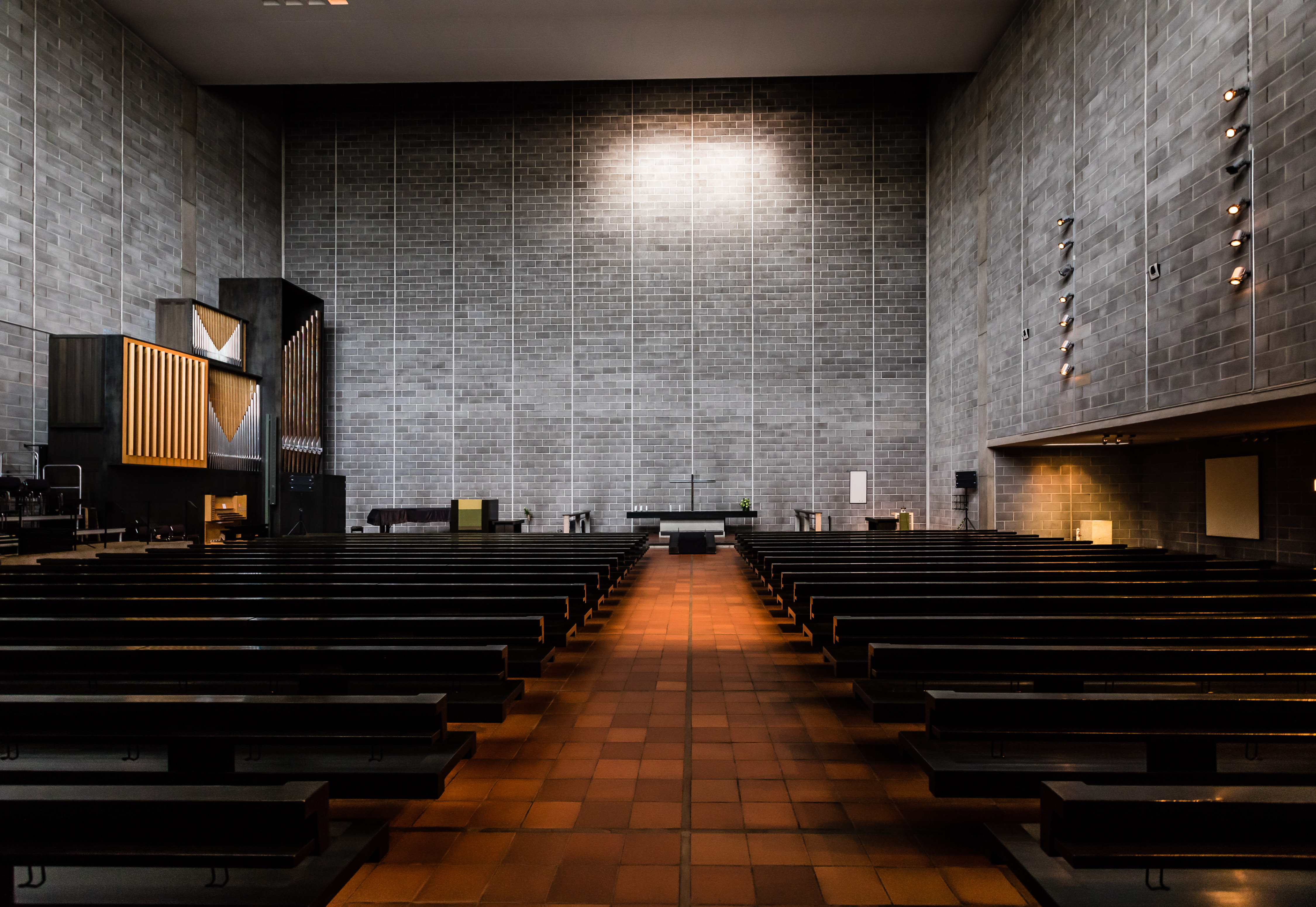 Kuvassa jylhä, avara kirkkosali, jossa harmaat betoniseinät, tiilenpunainen lattia ja mustat penkit.