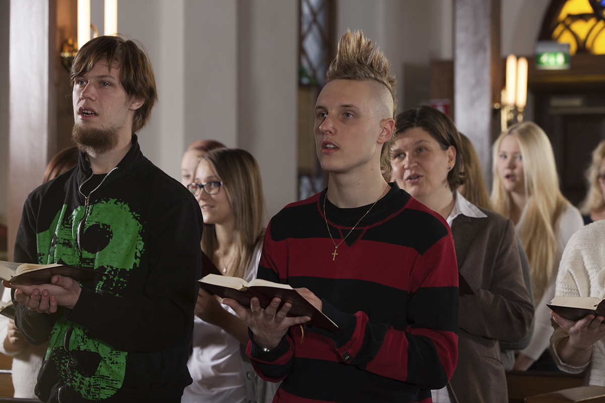 Kuvassa ryhmä eri-ikäisiä ihmisiä laulaa kirkkosalissa.