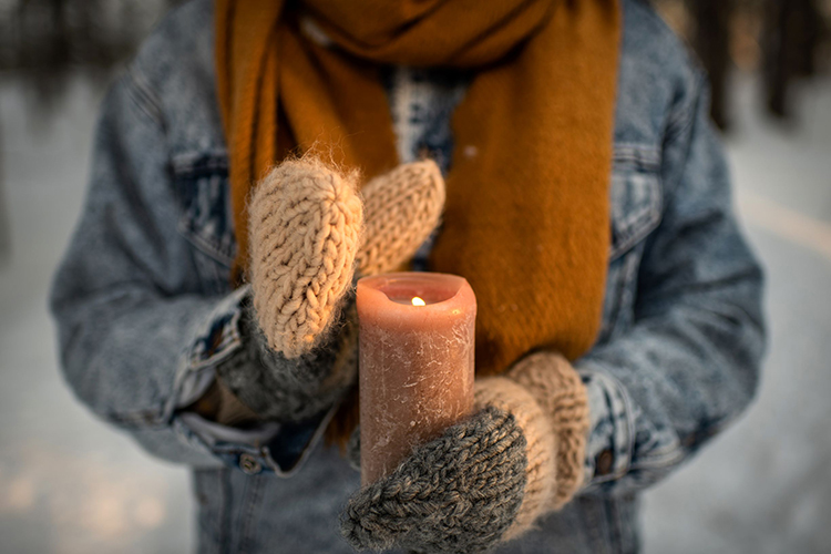 Henkilöllä on käsissään palava kynttilä. Käsissä on lämpimät lapaset.