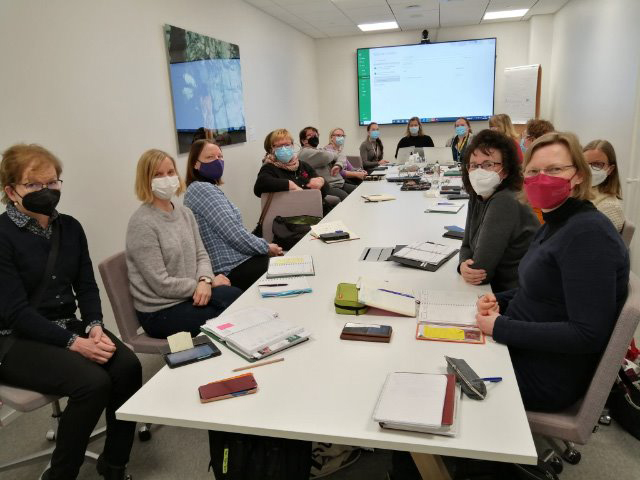 Kuvassa istuu ihmisiä neuvottelupöydän ympärillä maskit kasvoillaan.