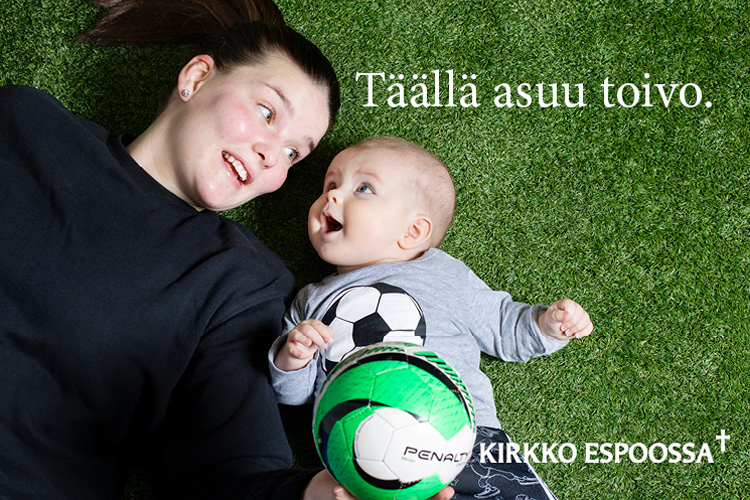 Kuvassa äiti ja vauva tekonurmella jalkapallon kanssa. Kuvassa lukee Täällä asuu toivo.