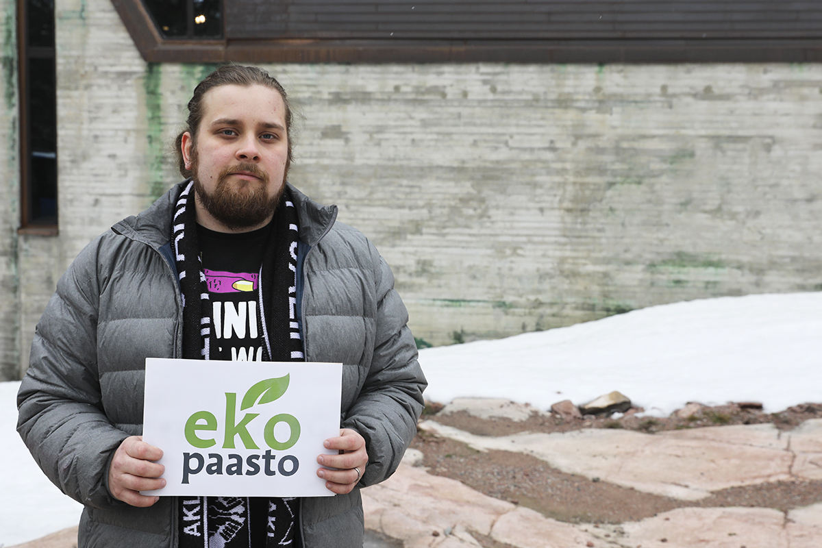Rasmus Tillander seisoo Espoonlahden kirkon kallioilla Ekopaasto-kyltti kädessään.