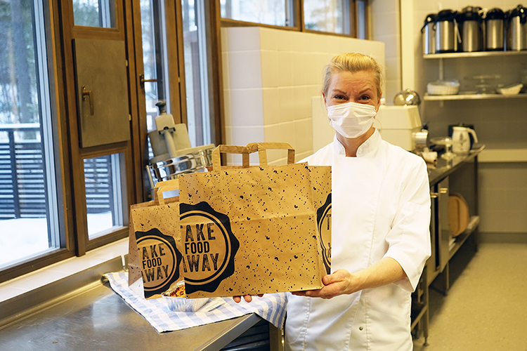 Kuvassa maskikasvoinen emäntä Merja Söderberg pitää käsissään take away -paperikassia.