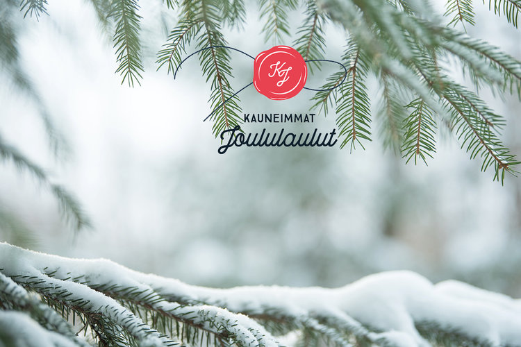 Kauneimmat joululaulut sinetinmuotoinen logo, taustalla lumiset kuusenoksat.