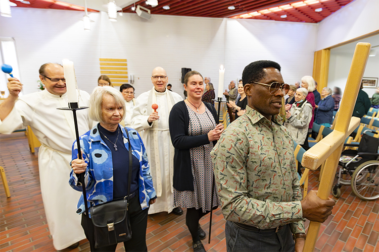 In the picture there are several people walking in the church, the first one is carrying a wooden cross.