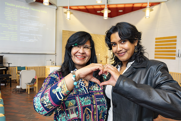 Two women, mother and her daughter are smiling and forming a heart with their hands.