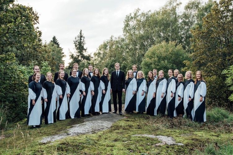 Ryhmäkuva kuorosta metsäaukiolla mustavalkoisisa esiintymisasuissa.