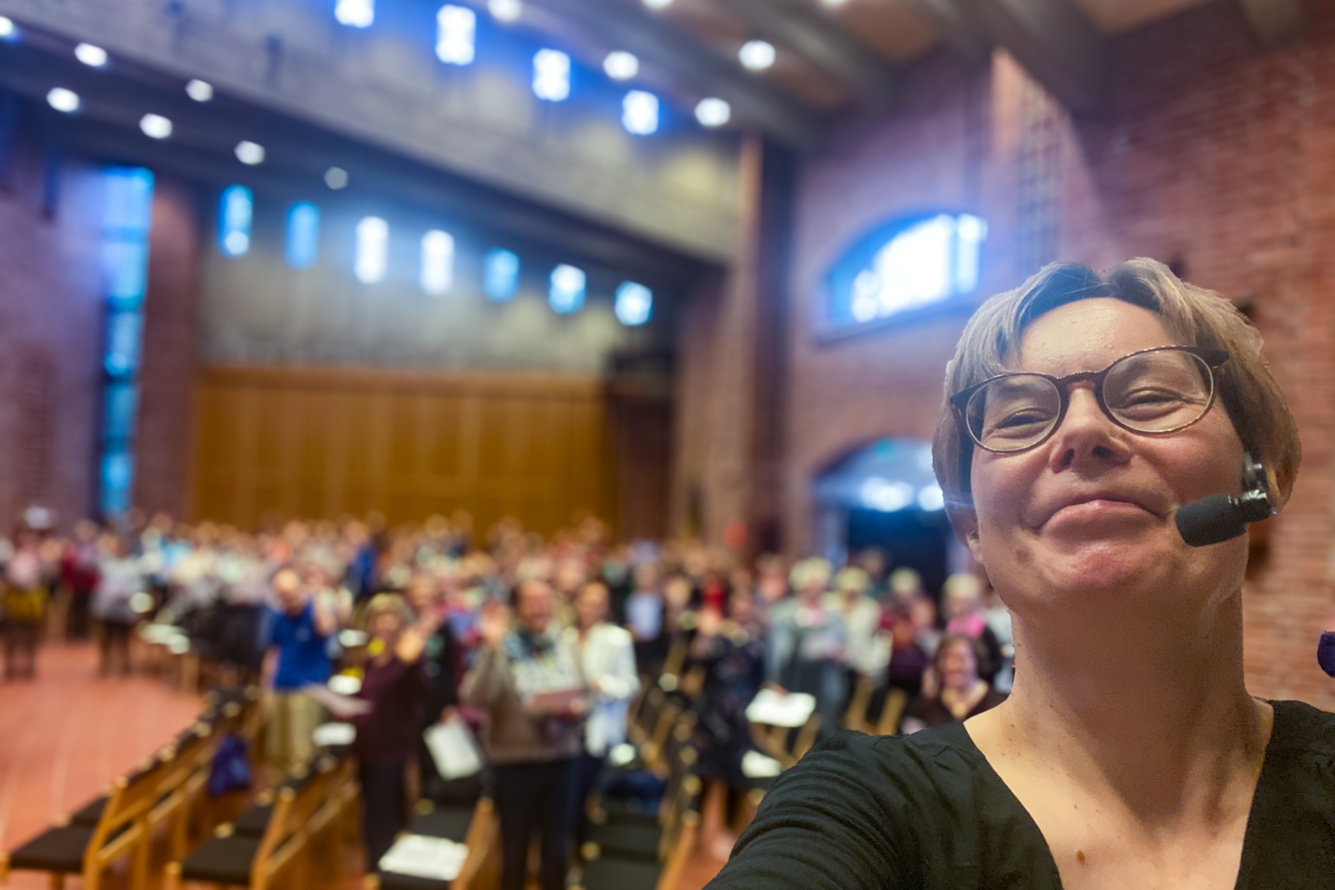 Kuoronjohtaja ottaa selfien, taustalla kirkkosali täynnä laulajia.