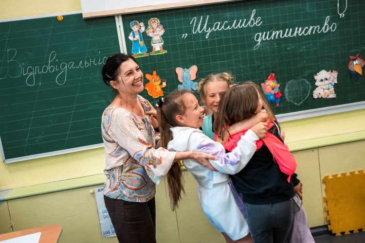 Opettaja ja ryhmä nuoria koululaisia iloisina koululuokassa.